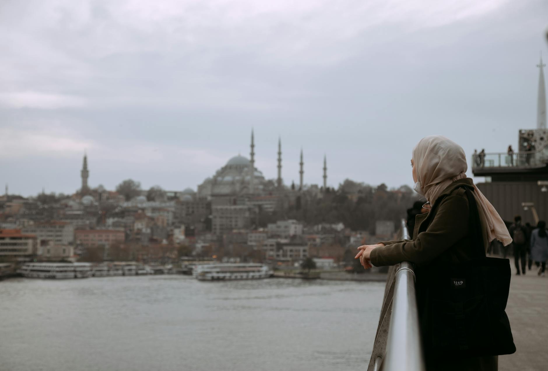 Mujer con velo apoyada en una barandilla observando el horizonte de Estambul, con la Mezquita de Süleymaniye visible en el fondo, un ícono del turismo en Estambul.